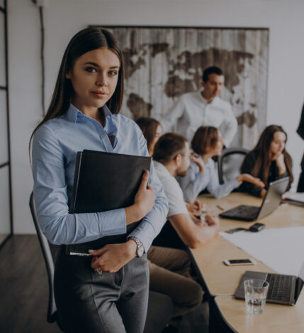 Elegant business-lady in trendy black jacket holding laptop and smiling. Portrait of cheerful blonde secretary and tall african office worker on background.